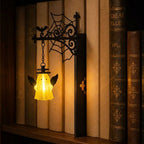 Geflügelter Geist als Bücherregal-Leuchte an einer dunklen, dekorativen Halterung mit einem Lichtakzent vor den Buchrücken.