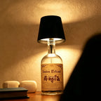 Tête de lampe BottleGlow noire sur une bouteille transparente, projetant une lumière chaude sur un mur
