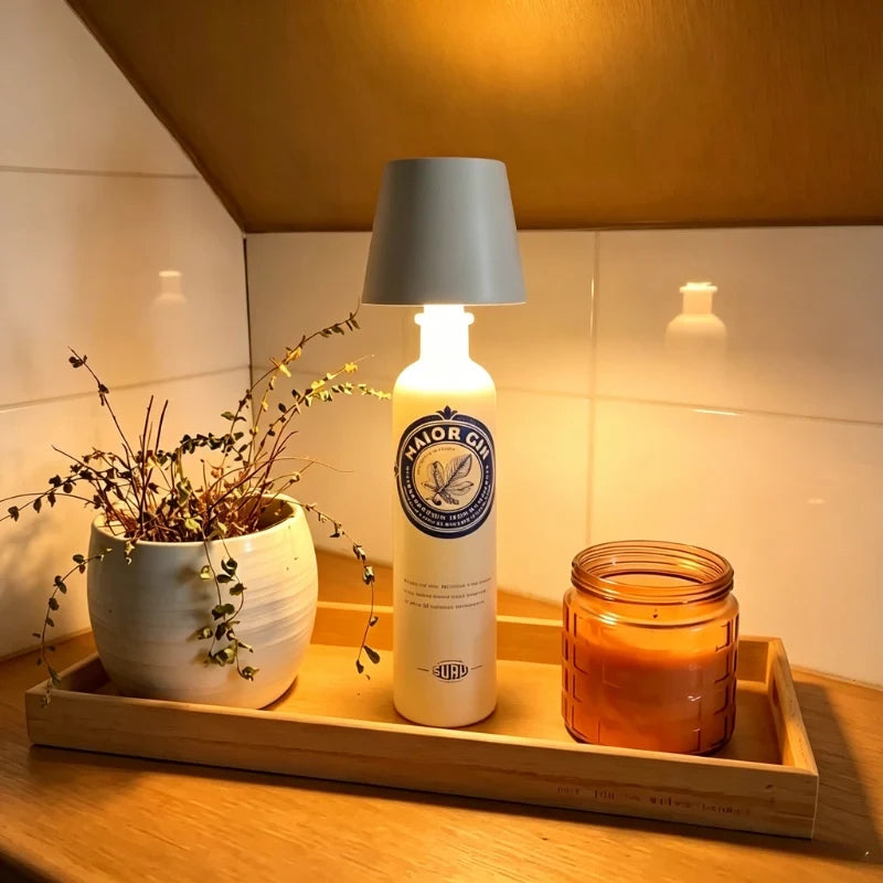 Tête de lampe BottleGlow grise sur une bouteille blanche à côté d'une bougie et d'une plante