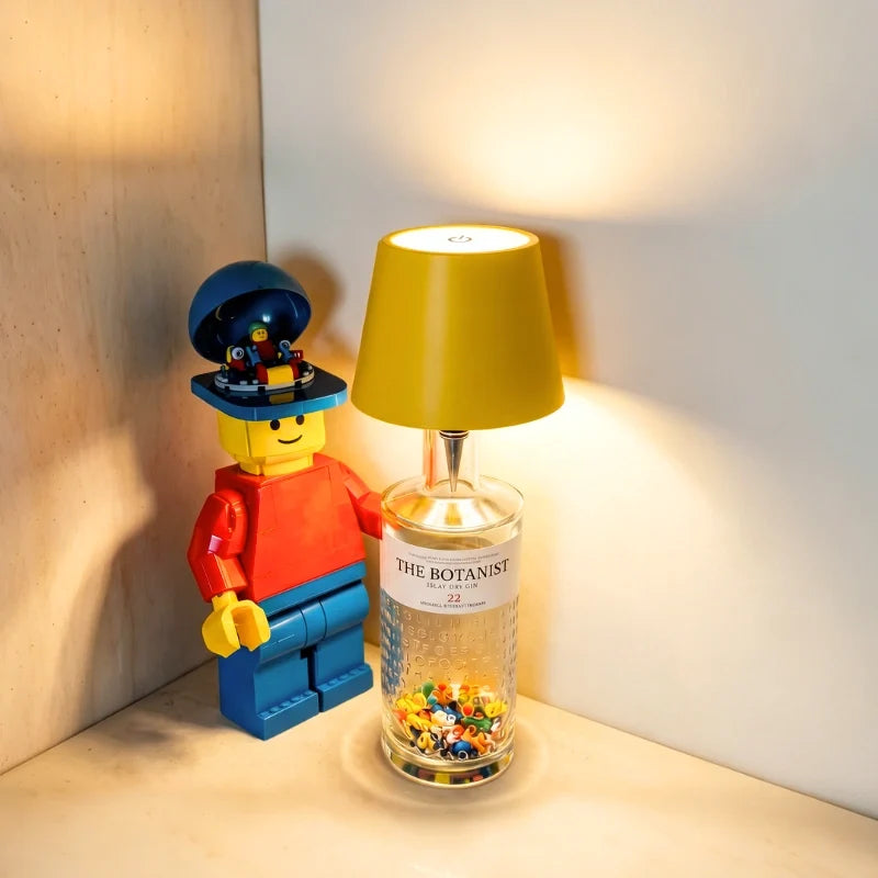 Tête de lampe BottleGlow jaune sur une bouteille transparente à côté d’une figurine colorée