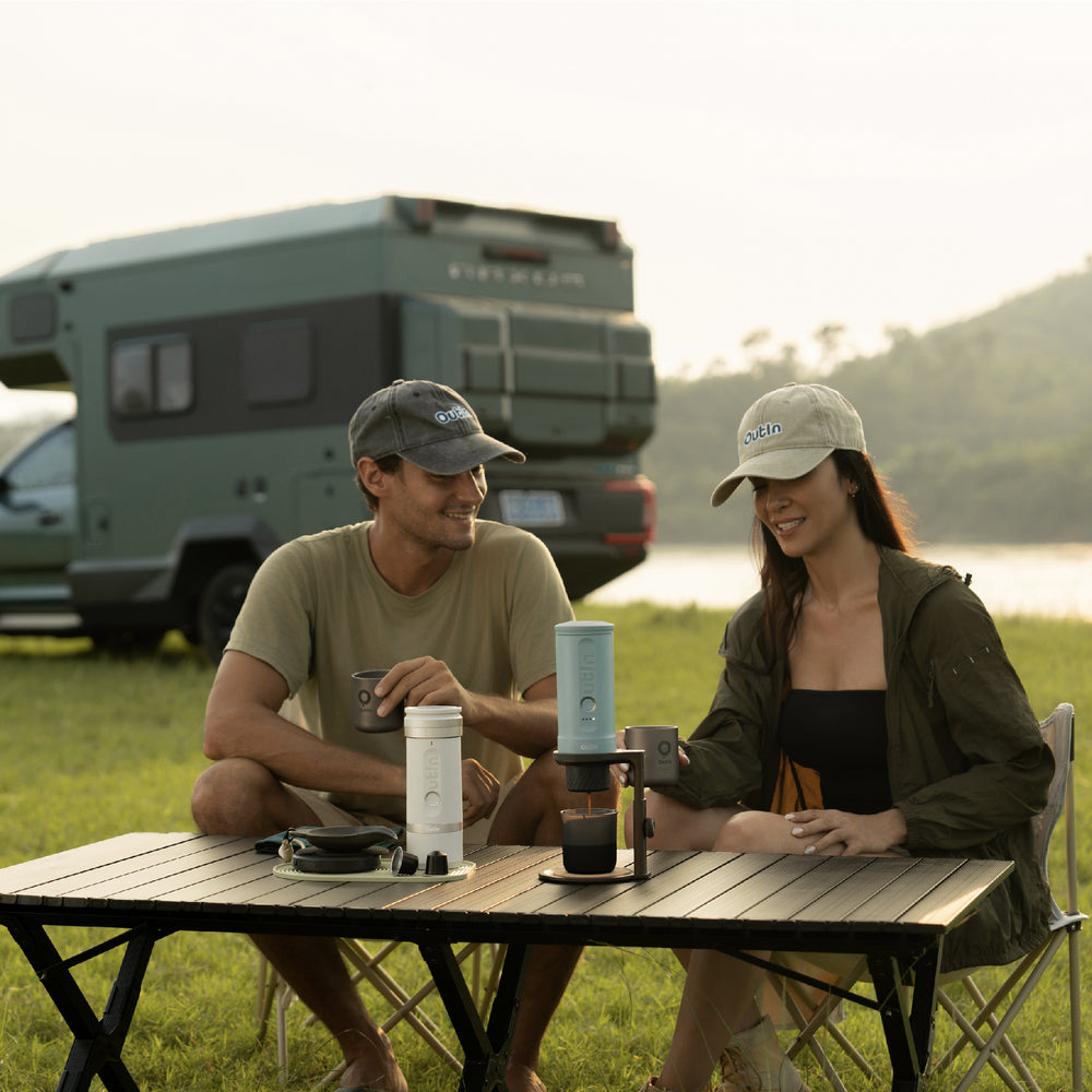 Two people using OutIn Nano 2 espresso machines at a campsite table